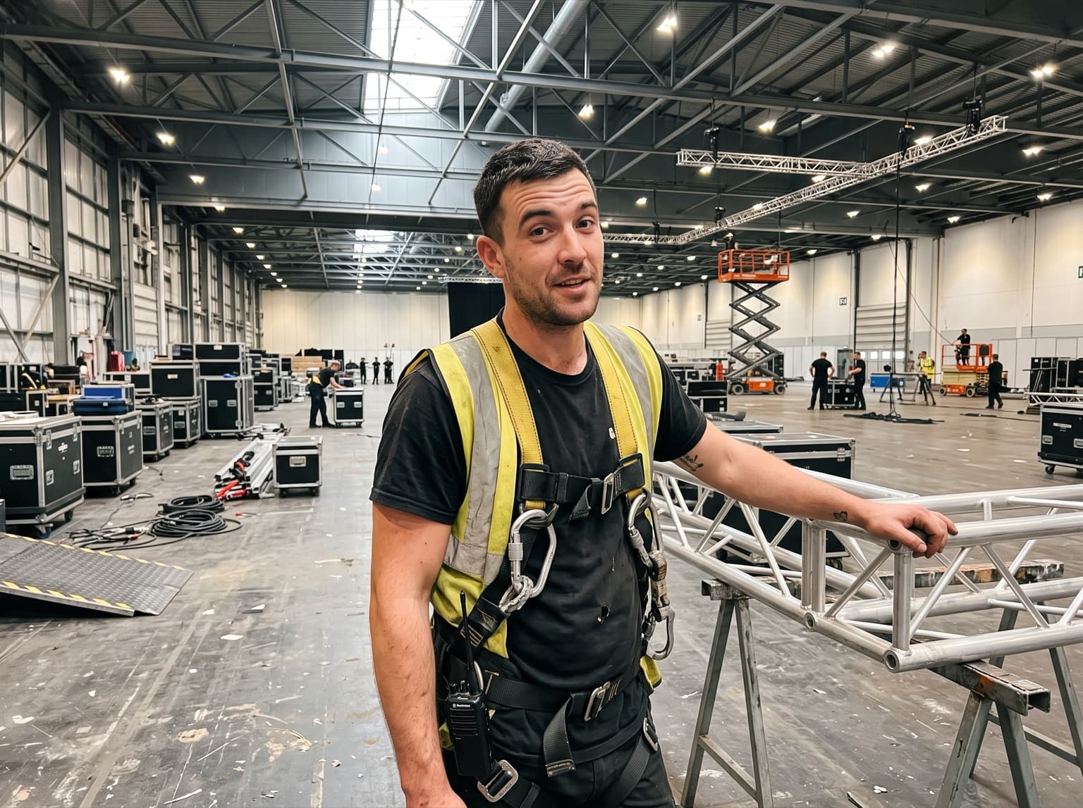 Events rigger in a harness beside a truss section in an exhibition hall on a build day
